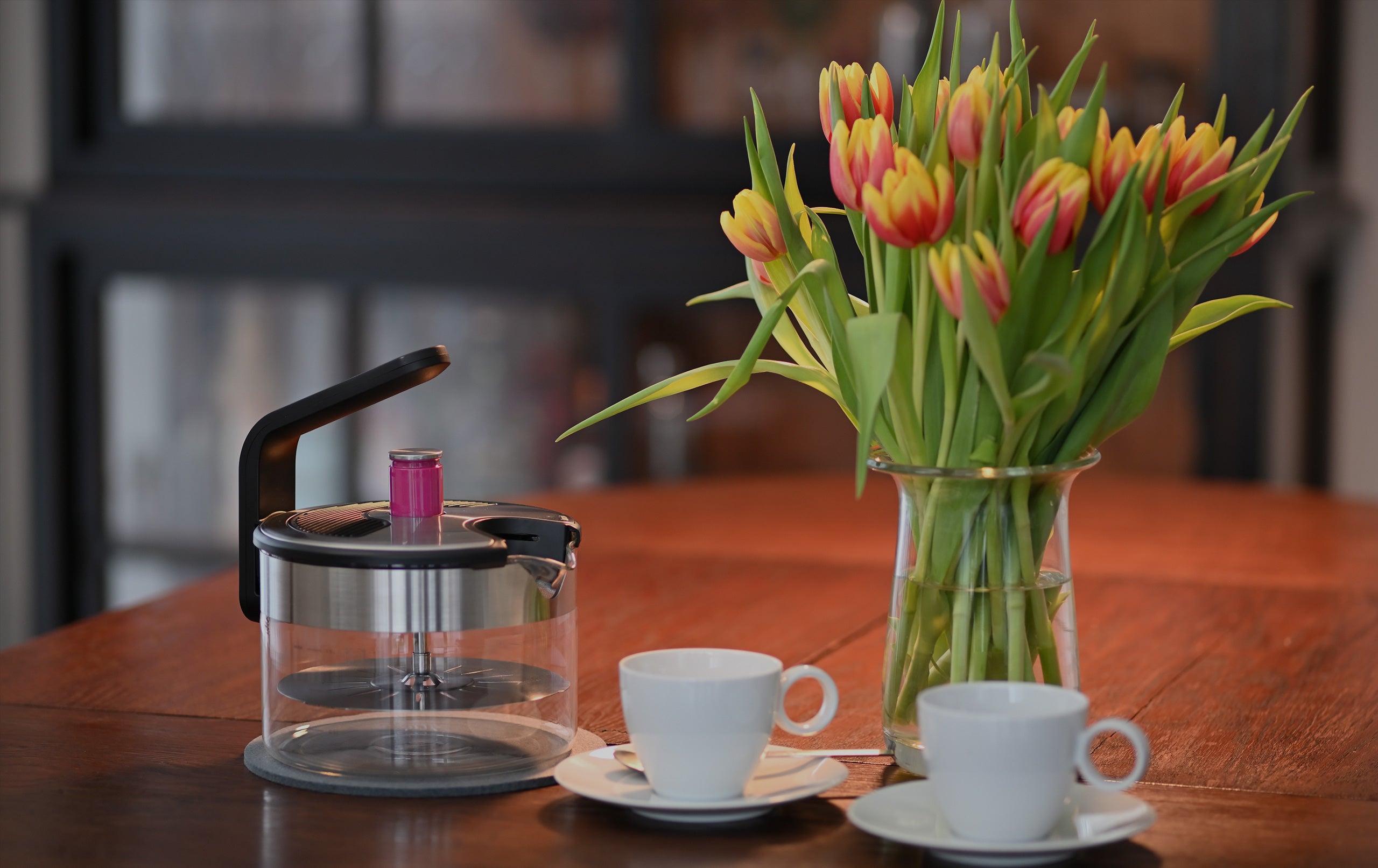 Der Kezzel steht dekorativ auf einem Tisch mit Blumen und Tassen.