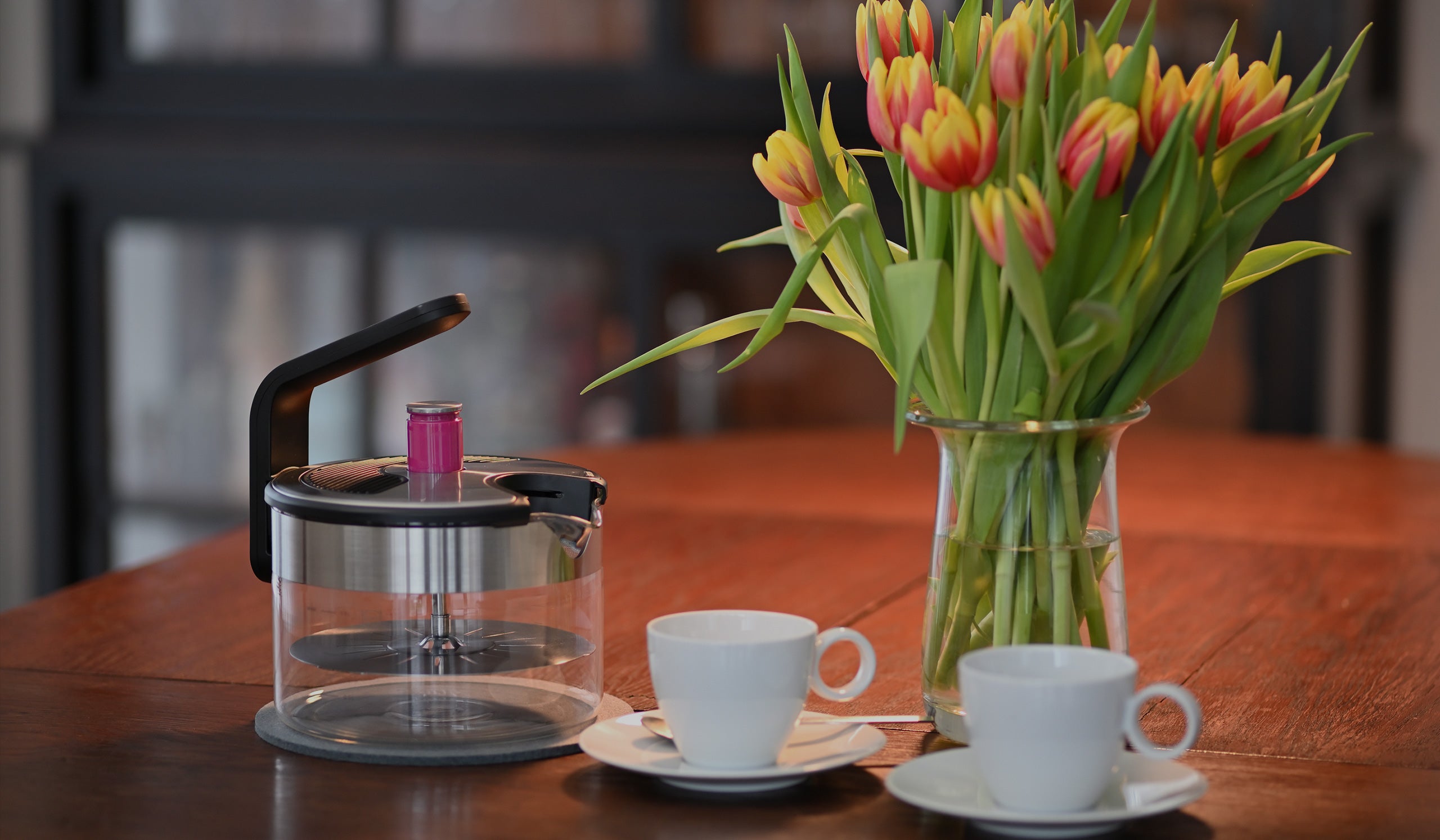 Der Kezzel steht dekorativ auf einem Tisch mit Blumen und Tassen.